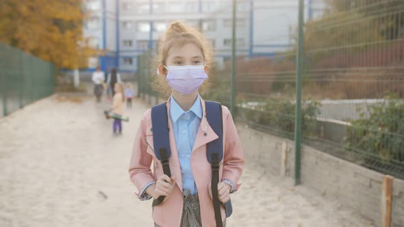 An 8Yearold School Girl Wearing a Protective Medical Mask Returns Home From School alt