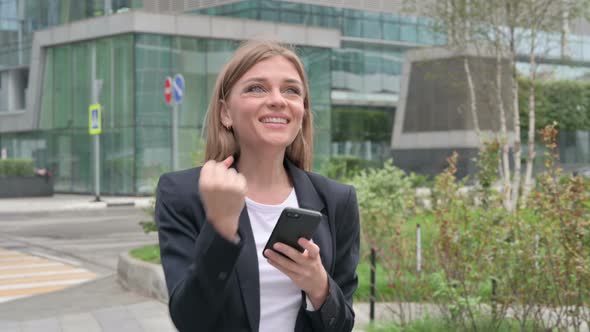 Young Businesswoman Celebrating Success on Smartphone While Walking on the Street alt