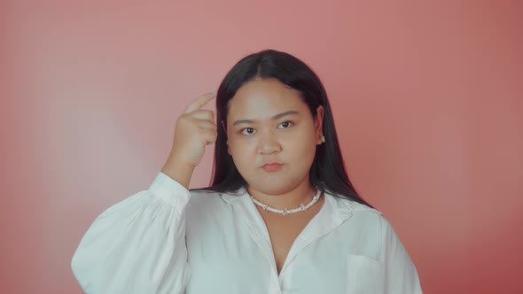 a Woman Shows She's Clever By Putting Her Finger to Her Head on a Pink Background alt