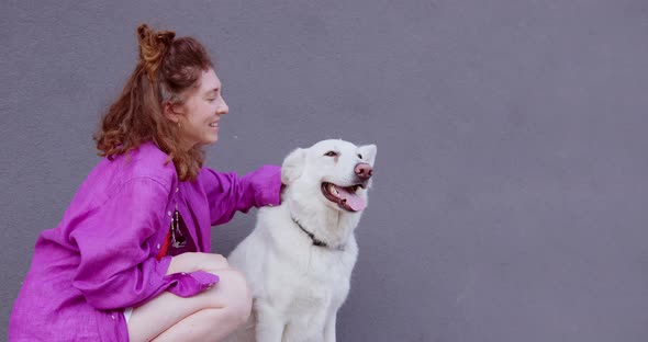 girl in pink shirt is petting a big white dog on the head and smiling alt