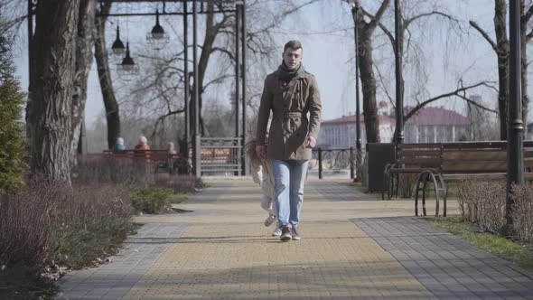 Active Little Caucasian Girl Running Around Tired Young Father. Cheerful Kid Jumping and Pulling Man alt