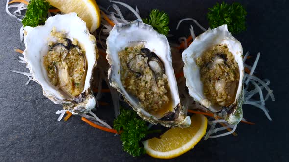 Cooked Oysters in Shell with Garlic and Lemon on Black Textured Slate Background alt