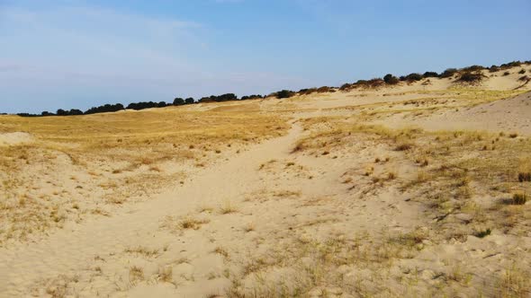 AERIAL: flying backwards over the sand dune and revealing clear blue sky alt