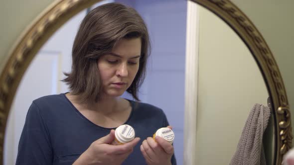 Depressed woman looking at two prescription bottles alt