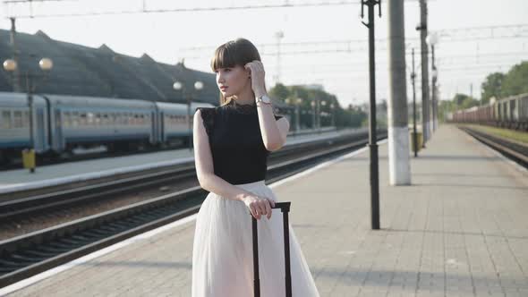 Glamorous Model in Blackwhite Dress Poses with Red Suitcase on Railway Platform alt
