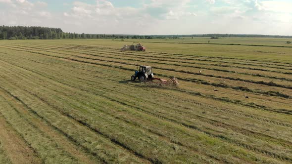 Picturesque Landscape with Several Tractors Mowing and Removing Fresh Grass for Animal Feed alt