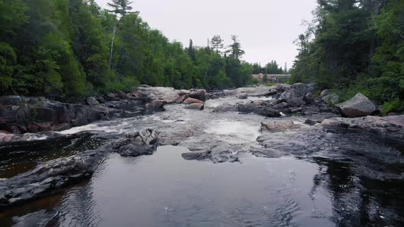 Drone footage flying quickly low near the water in a river surrounded by trees in a forest with many alt
