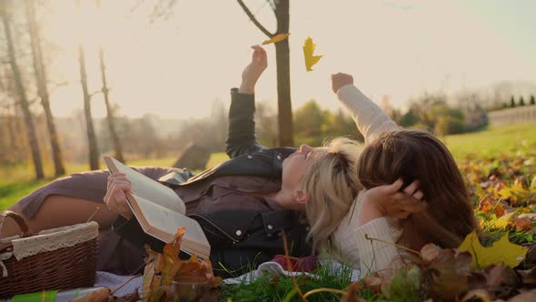 Mother and daughter laying at autumn park outdoors and reading a book. Two females persons alt