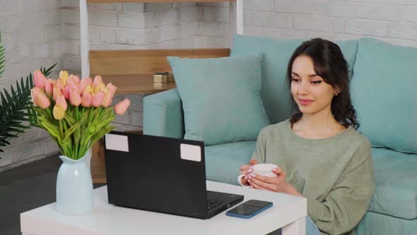 Girl Sits on Floor Carpet and Use Computer to Watch Movie and Drink Tea alt