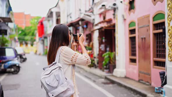 Young woman traveler walking and taking a photo at Phuket old town in Thailand