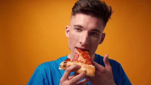 Close Up of a Guy Eating Pizza Slice Against Yellow Studio Background alt