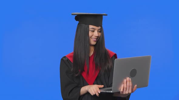 Portrait of Female Student in Graduation Costume Talking for Video Chat Using Laptop and Rejoice alt