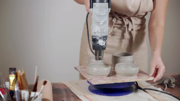 Woman Is Drying Ceramic Blanks of Bowls By Electric Dryer, Close-up of Hands alt