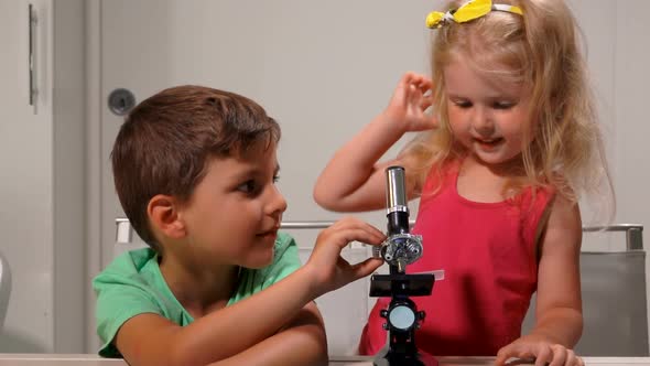 Cute Blond Little Girl and Boy are Sharing a Microscope with Each Other alt