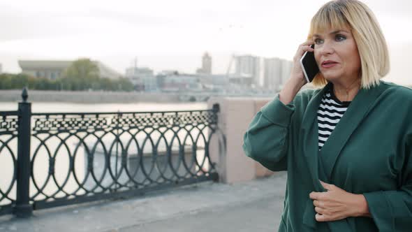 Beautiful Woman Speaking on Mobile Phone Walking Outdoors Along River Embankment alt