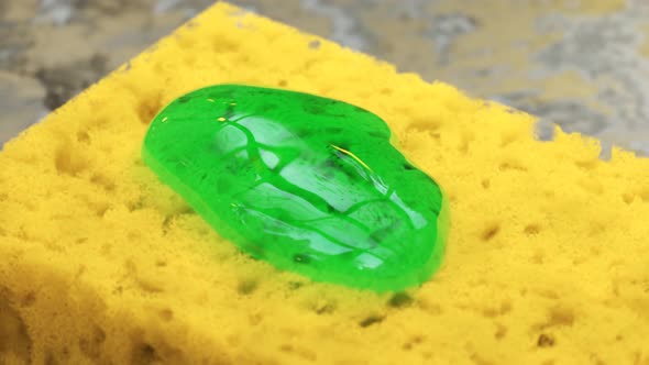 Squeezing green liquid dishsoap detergend on a yellow sponge. Kitchen cleaning