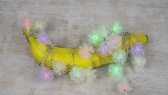 Banana Wrapped In Blinking Lights On A White Wood Board