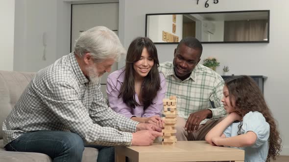 A Multiethnic Family of Different Age Generations is Playing a Board Game at Home Removing Wooden alt