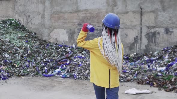 Woman in Hard Hat Standing Against the Pile of Broken Glass Used Bottles Next to the Wall alt