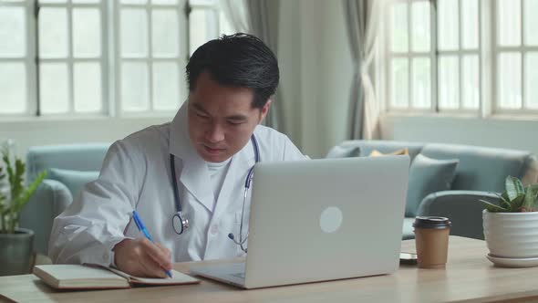 Asian Male Doctor Working On Laptop Computer And Write On Note Book At Home Office alt
