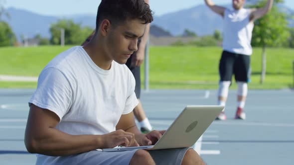 Teen basketball player using laptop computer at outdoor court