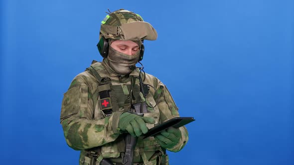 Modern Soldier in Camouflage on the Blue Chroma Key Military Engineer Uses a Digital Screen Tablet alt