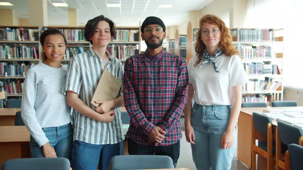 Slow Motion Portrait of Joyful Students Standing in Library Holding Books alt