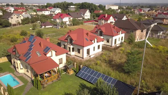 Aerial View of a Residential Private House with Solar Panels on Roof and Wind Generator Turbine alt