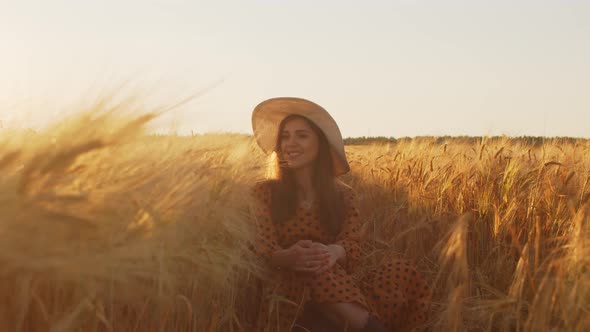 Pregnant woman in the rays of the sunset in the field alt
