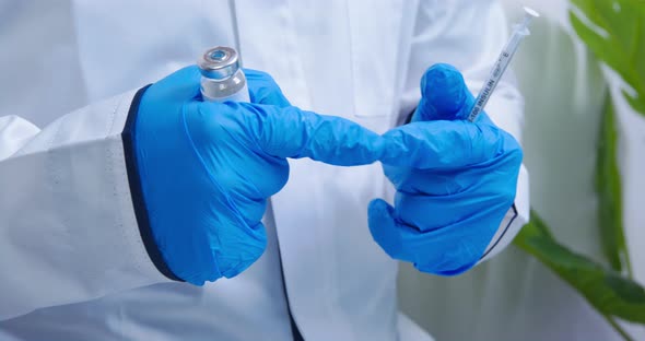 Doctor Wearing Sterile Rubber Gloves Holds a Vial of Vaccine and Syringe with Needle and While