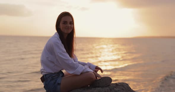 Young Woman Showing Let It Rock Gesture Sitting Near Sea alt