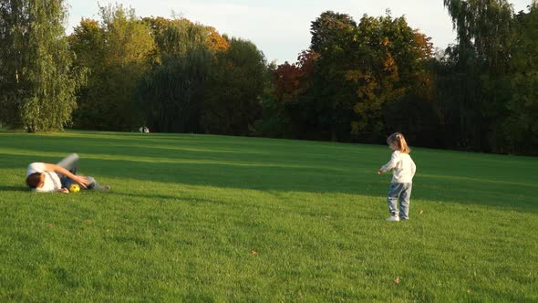 Father and Little Girl Play Soccer Ball on Green Lawn in Summer Park
