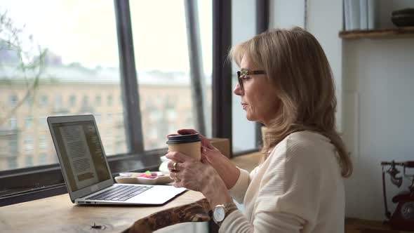 Businesswoman Working with Laptop and Drinking Coffee at Table in Modern Home Office alt