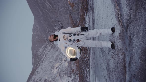 Astronaut Stands with a Helmet in His Hand By the Hills alt