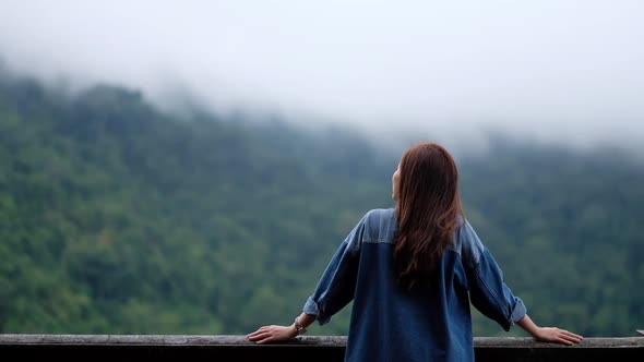 Rear view of a female traveler looking at a beautiful green mountain on foggy day