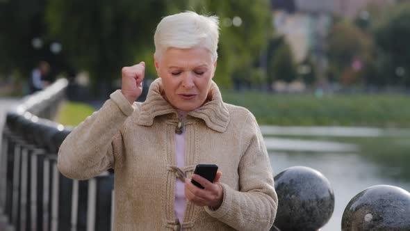 Euphoric Grayhaired Mature Woman Looking at Cellphone Screen Reading Sms with Unexpected Excellent alt