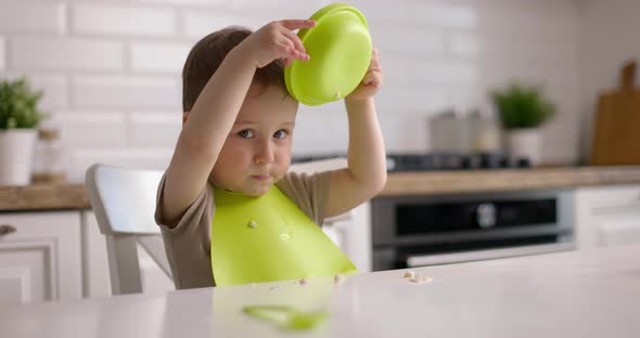 Small Cute Baby Boy Sitting at a Table and Plays with Green Dishes alt