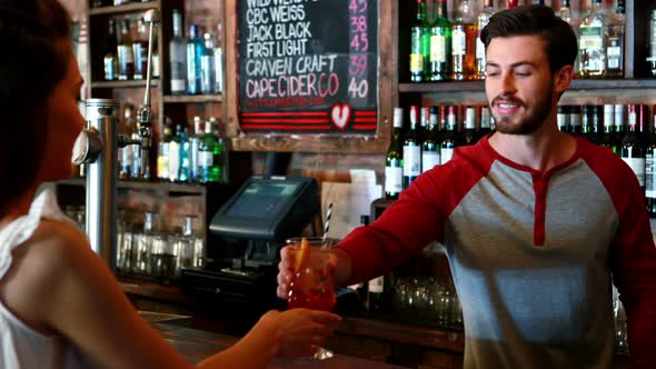 Barman interacting with female costumer while serving cocktail alt