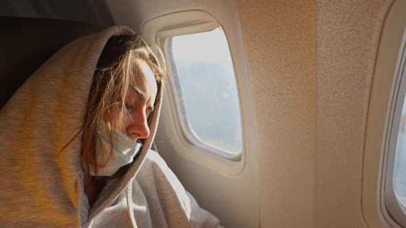 Tired Female Airline Passenger in Covid Safety Face Mask Sleeping in Seat at Window alt