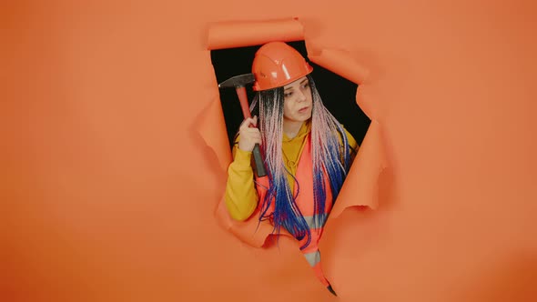 A Female Construction Worker Thinks and Scratches Her Helmet with a Hammer Trying to Remember alt