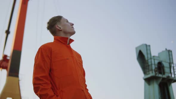 Handsome Young Container Warehouse Worker in Orange Uniform Standing By the Ship at the Harbor alt