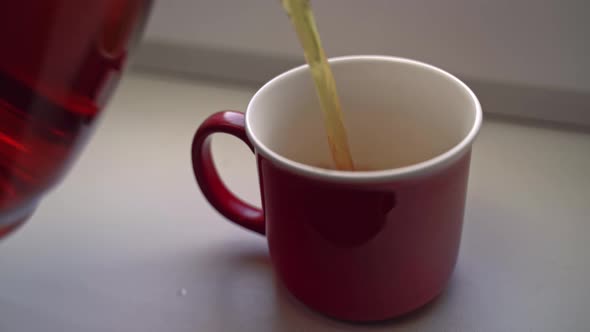 Man Pours Tea From Glass Teapot Into Red Ceramic Mug