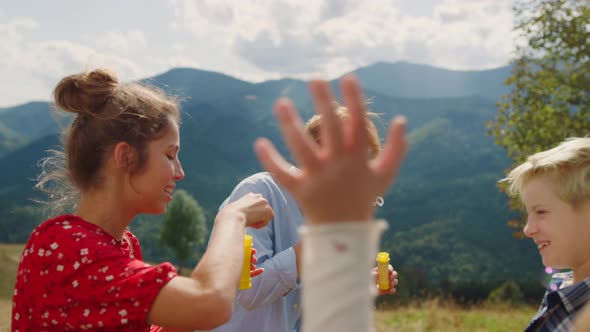 Family Playing Blowing Soap Bubbles in Summer Mountains alt