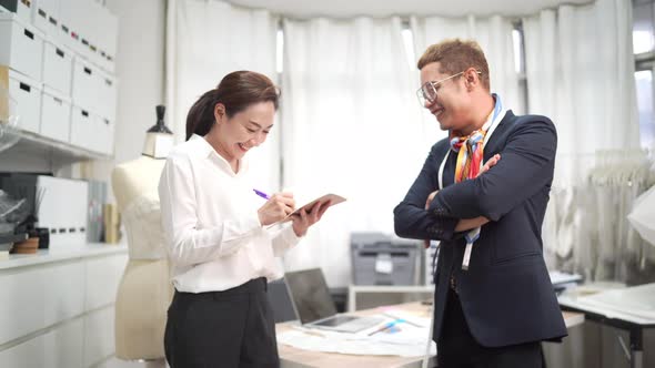 4K Asian bridal shop owner working with female assistant and talking on phone with customer alt