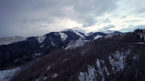 Panning drone shot of large snowy mountain peaks with a winding road alt