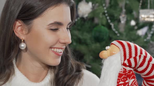 Cheerful Woman Smiling to the Camera Holding Toy Sant Claus alt