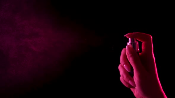 Woman's Hand Finger Sprays Perfume on Black Background with Pink Neon Light alt