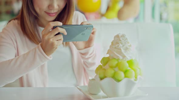 Young woman taking photo of bingsu with smart phone in restaurant