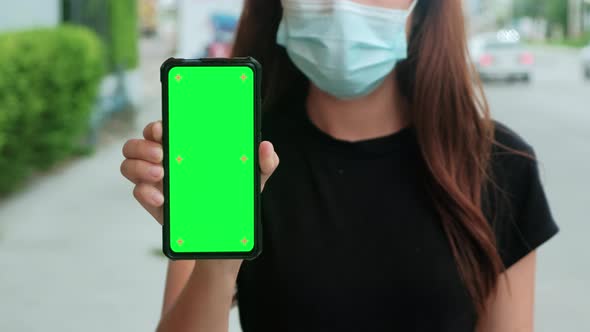 Asian woman with medical mask standing on city shopping street, holding a phone with a chromakey