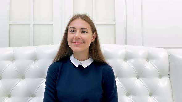 Beautiful smiling girl sitting on a white sofa and looking at the camera